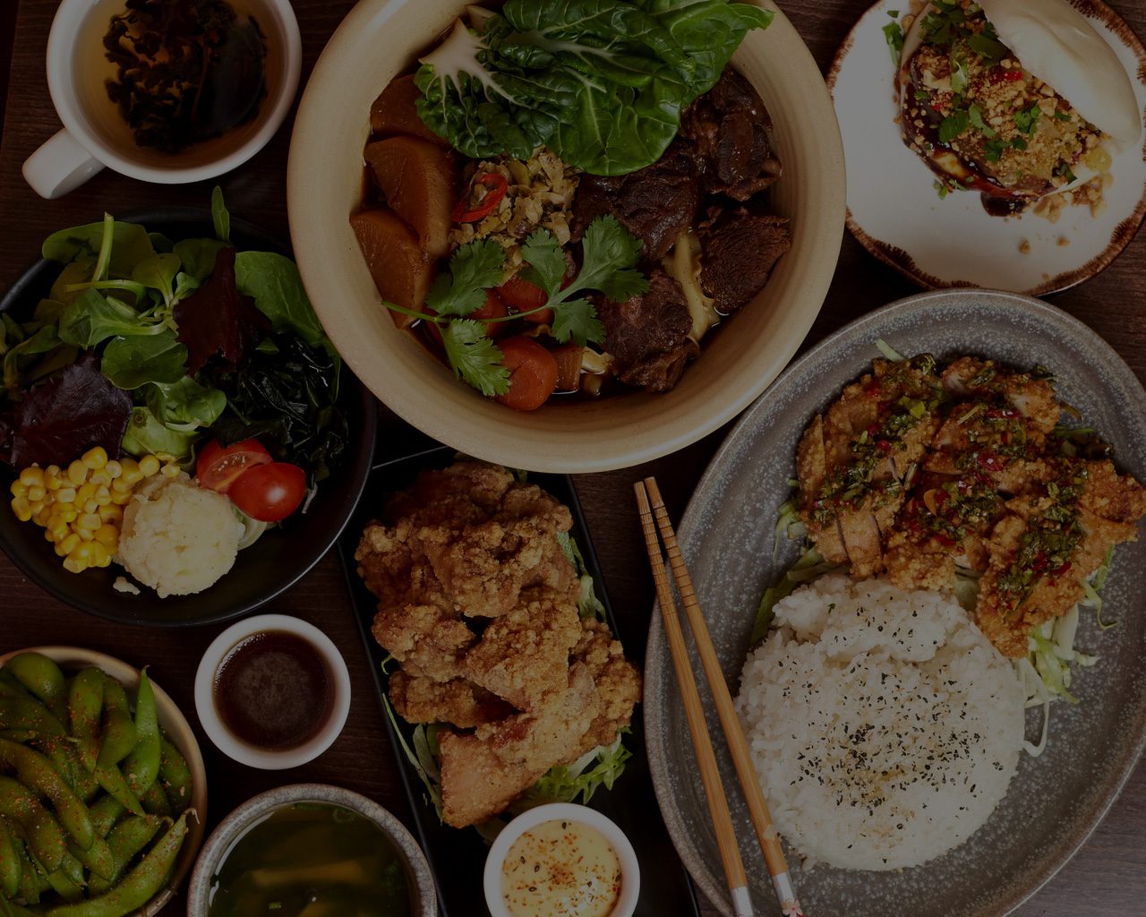 Overhead view of BaoBao dishes: beef noodle soup, braised pork rice, fried chicken and edamame