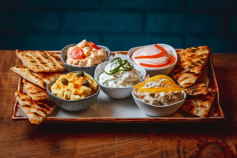 Five Greek dips served on a board with grilled pitta