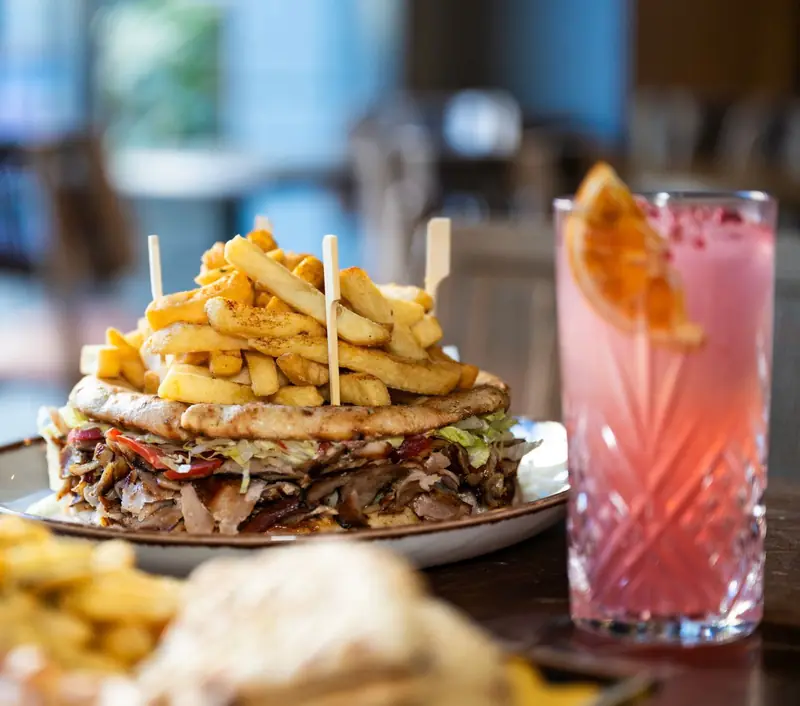 Pitta club topped with a tower of chips, next to a pink cocktail