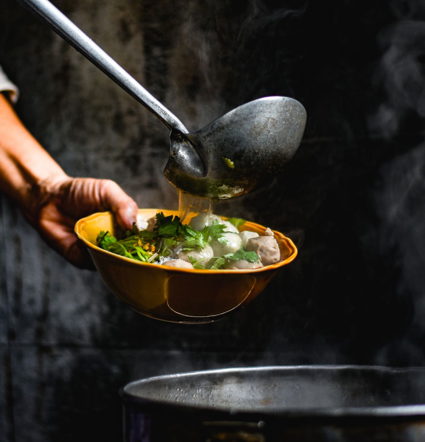 Broth being ladled into a bowl of noodles