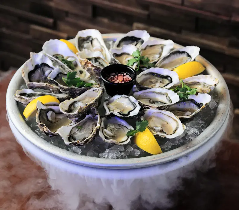 Two dozen raw oysters on a stand of crushed ice with lemon and shallot vinegar