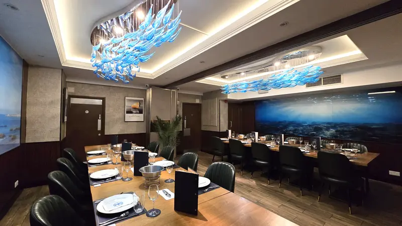 Private dining room with long tables, green leather chairs, blue glass fish chandeliers and an underwater mural