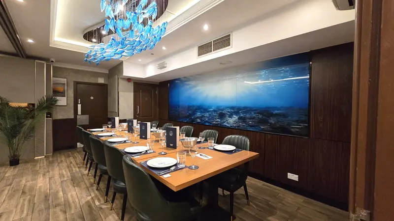 Private dining room set for twelve, under a blue glass fish chandelier, facing a wall-sized underwater mural